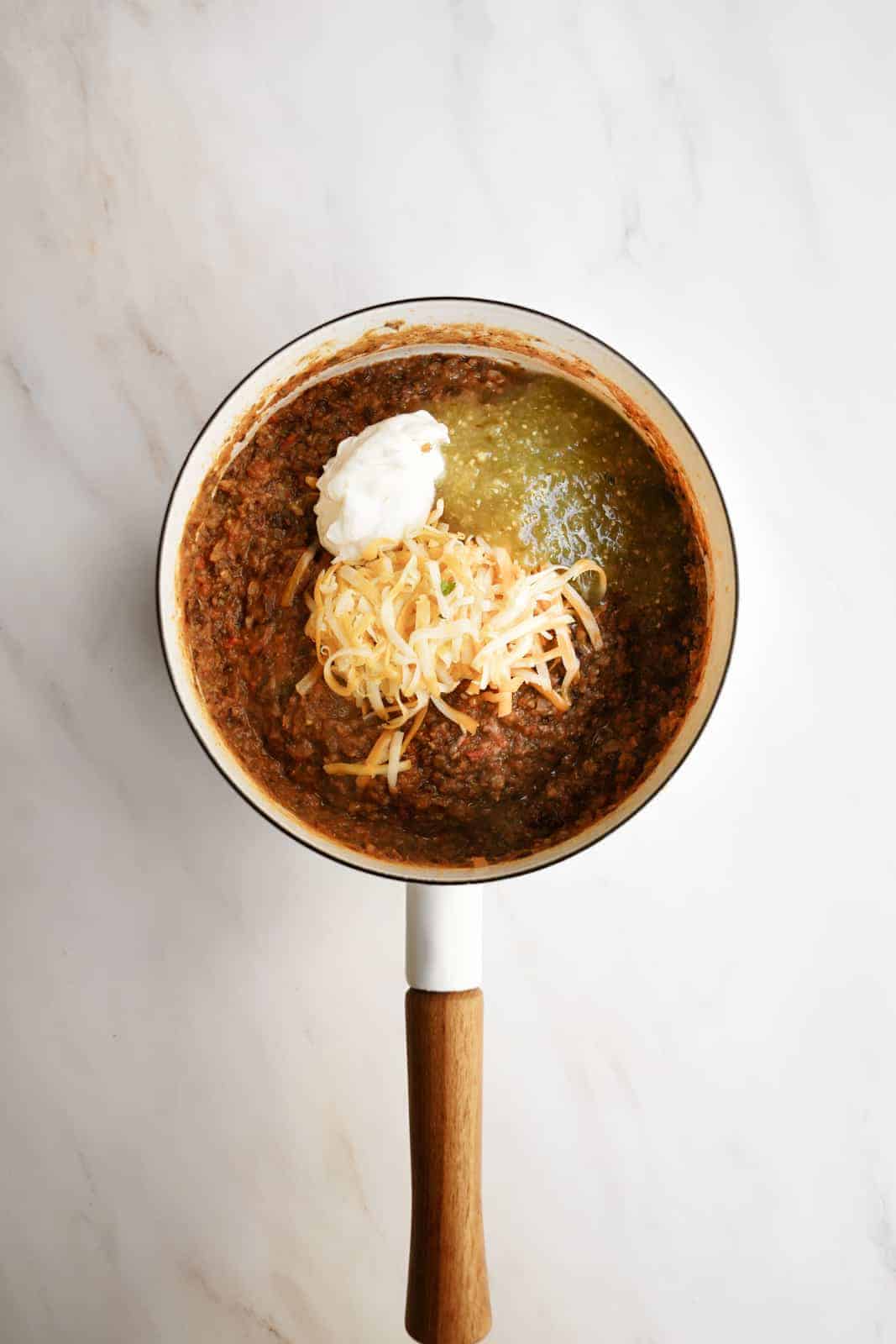 Black Bean Dip ingredients in a pot topped with cheese, salsa, sour cream