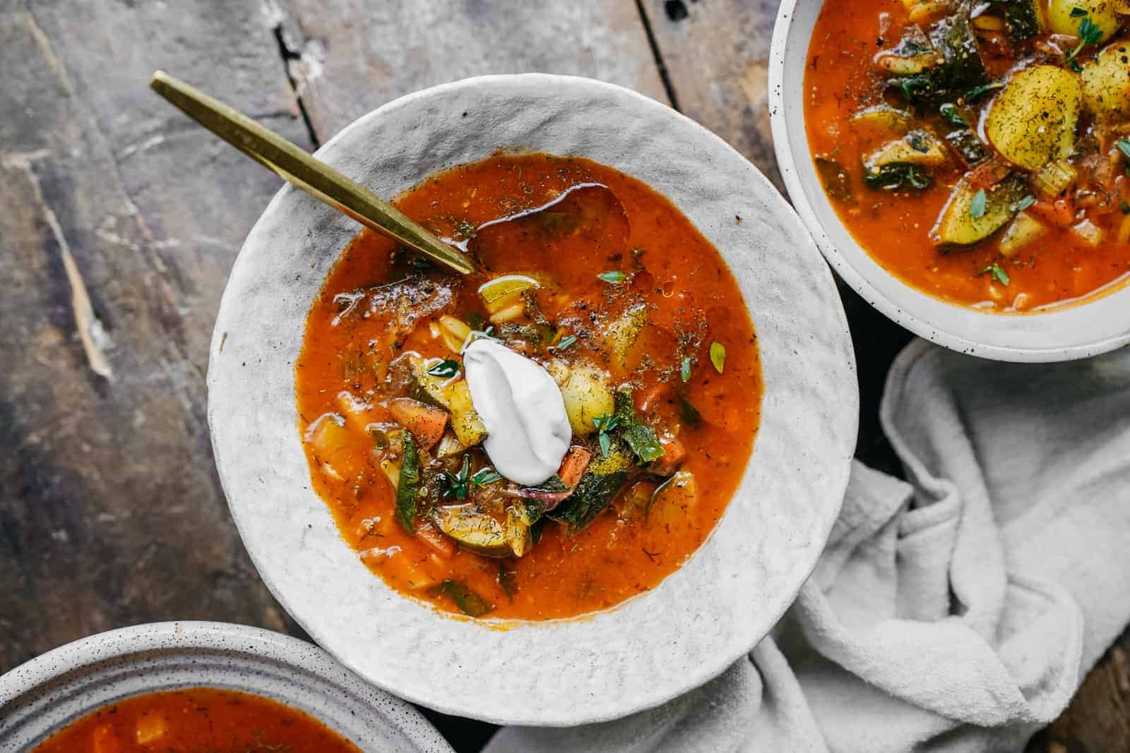 Bowls of vegetable orzo soup on wood table.