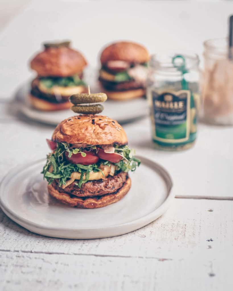 A gorgeous stacked burger on a plate with vegan big mac sauce on it.