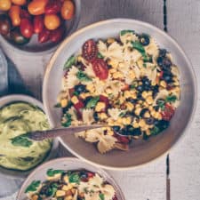 Bowl of Vegan Pasta Salad surrounded by fresh vegetable ingredients