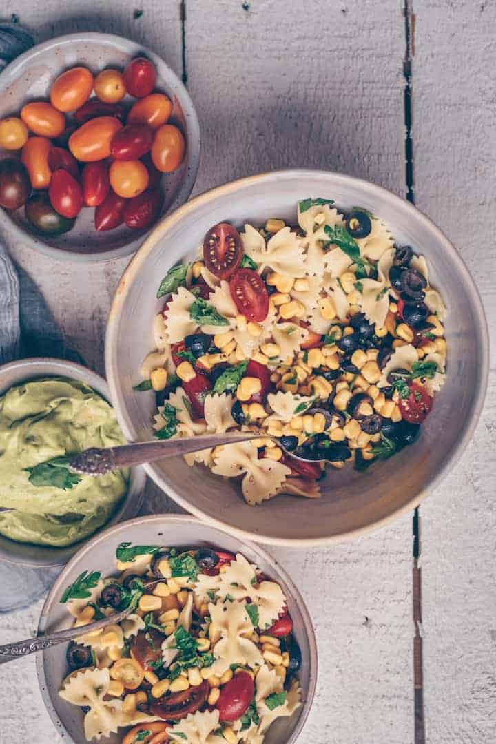 Bowl of Vegan Pasta Salad surrounded by fresh vegetable ingredients