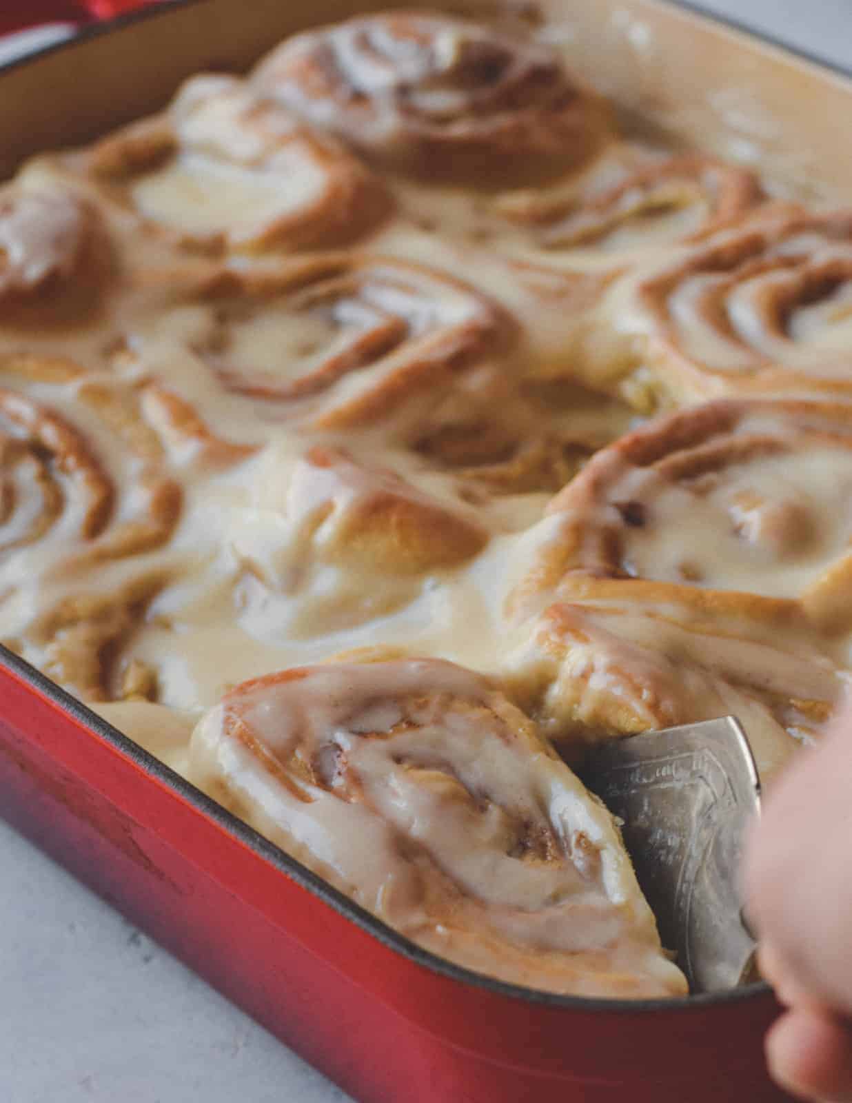 Casserole dish of sticky cinnamon rolls being cut into pieces
