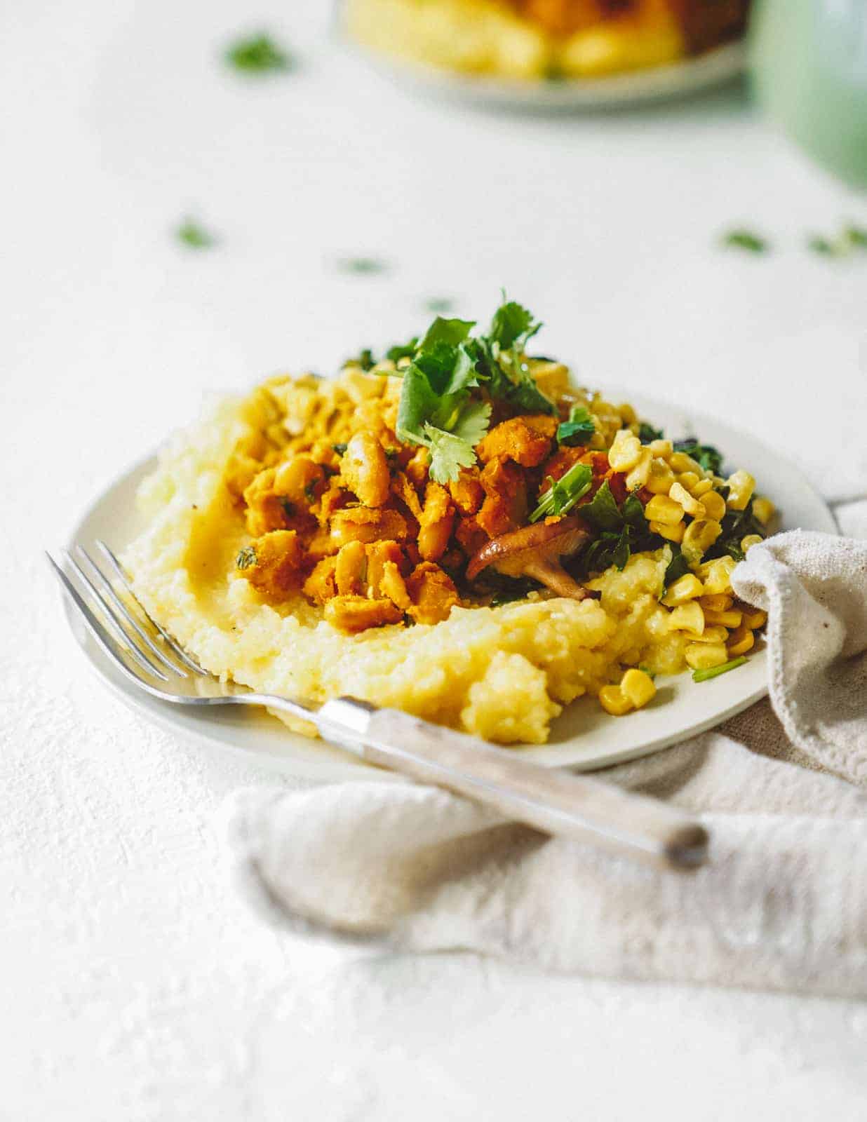 Vegan grits with collard greens in a serving dish on a white table.