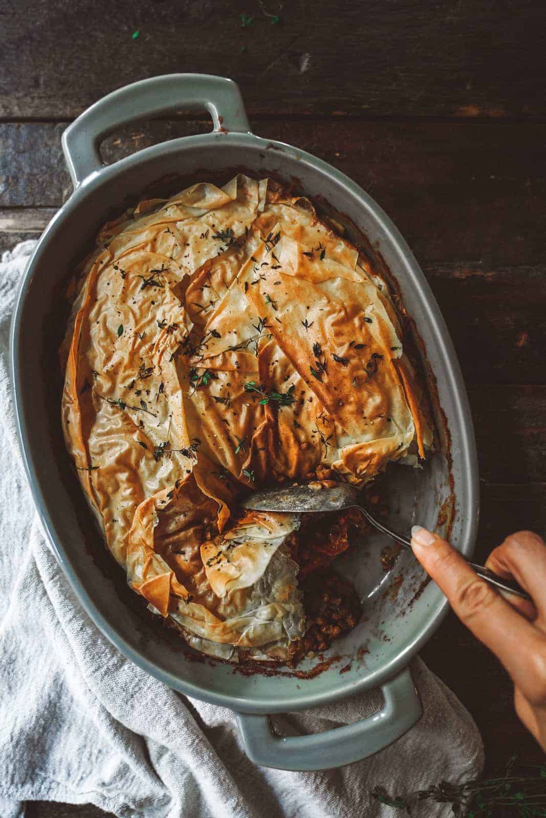 Looking for one of the most comforting recipes to make this September? This phyllo pastry casserole is just that. Big casserole dish on wood table with spoon digging into casserole.