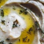 Close-up of creamy onion garlic mashed potatoes swirled with olive oil and garnished with fresh thyme leaves. The smooth texture and infused flavors paired with the golden oil create a visually appealing dish.