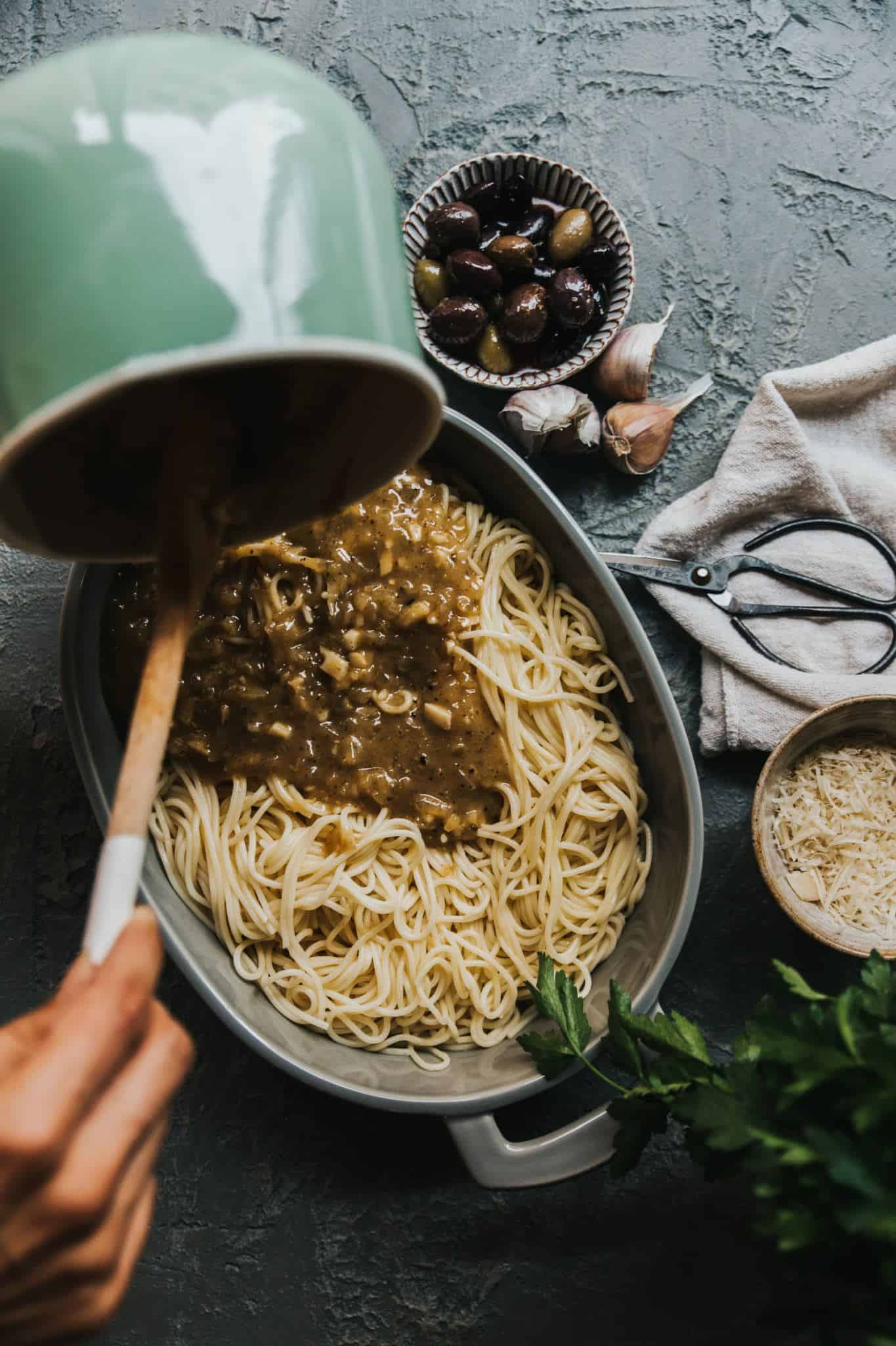 The creamy vegan truffle garlic sauce being poured onto the cooked spaghetti.