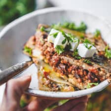 Big bowl of vegan moussaka ready to be eaten with fresh vegan feta and herbs.