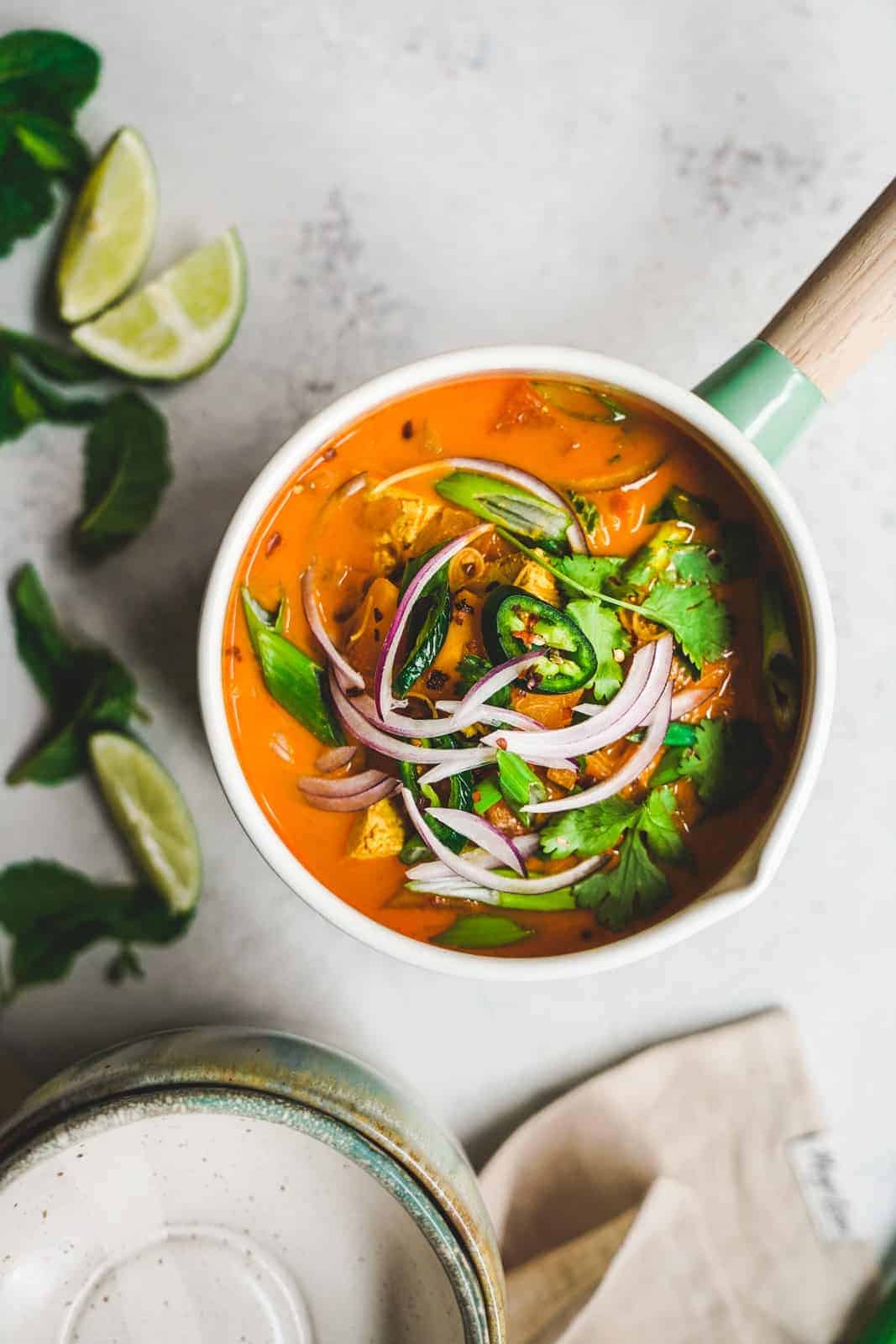 Side angle of colorful one pot vegan curry noodle soup with fresh ingredients on top.