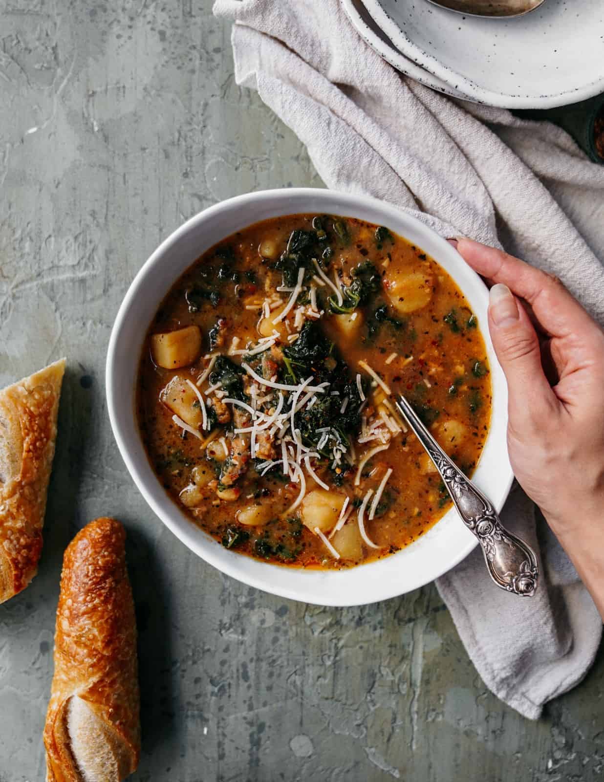 Italian Zuppa Toscana turned vegan in a white bowl with a spoon next to some bread