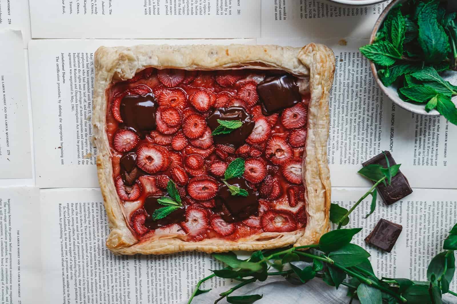 Beautiful strawberry tart on counter, surrounded by herbs. This is a great vegan easter recipe for brunch or dessert.