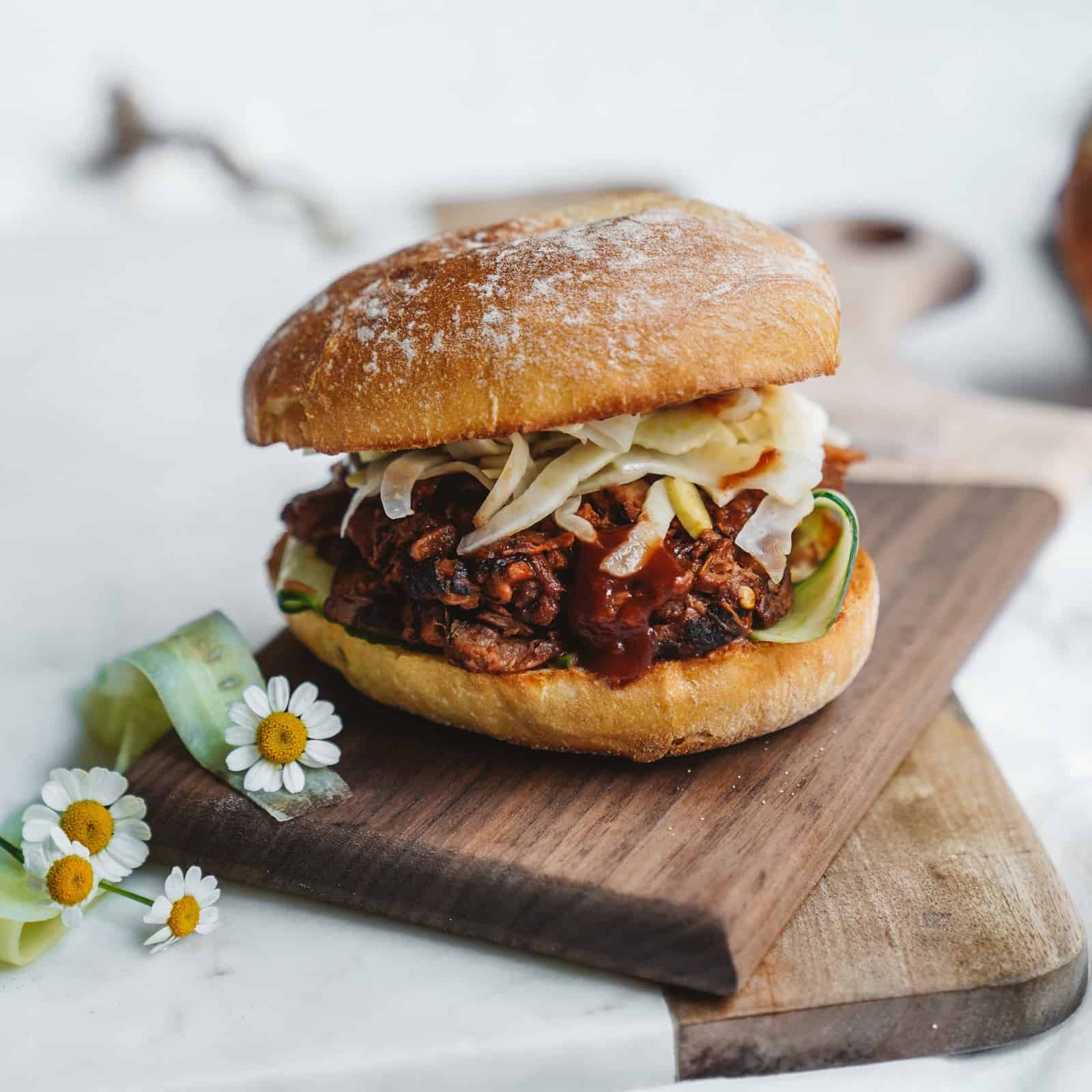 Side view of a delicious jackfruit burger patty stacked on a cutting board and topped with fennel coleslaw.