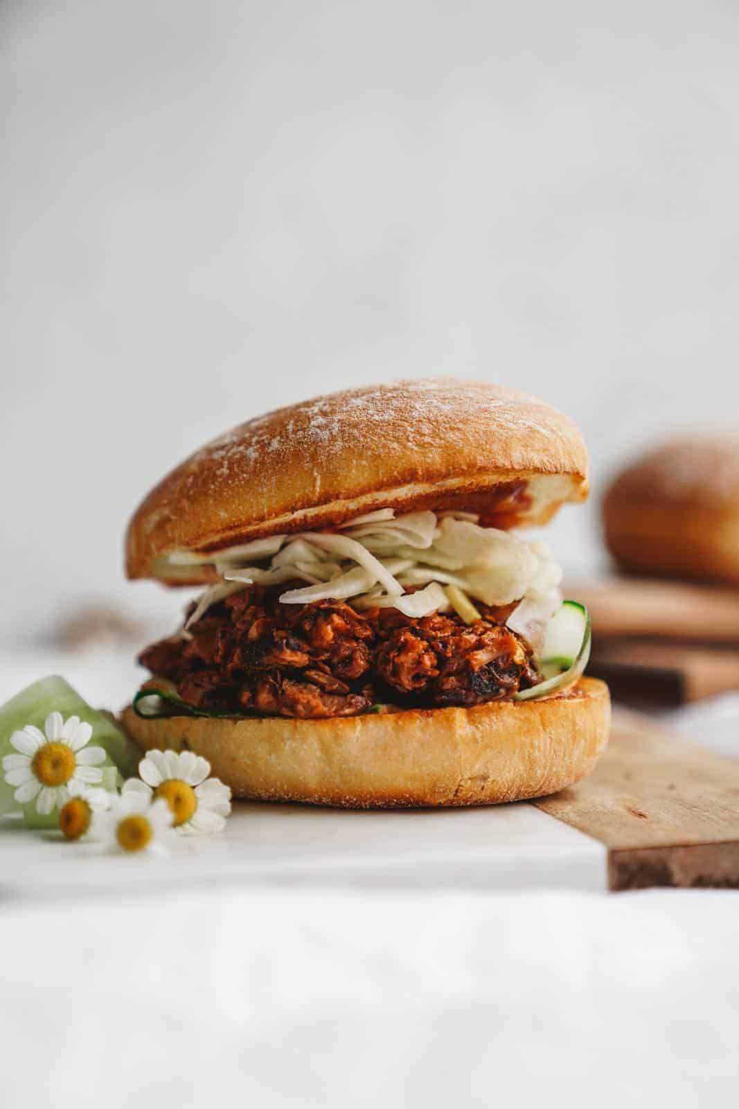 A jackfruit pulled pork burger sitting on cutting board with flowers.