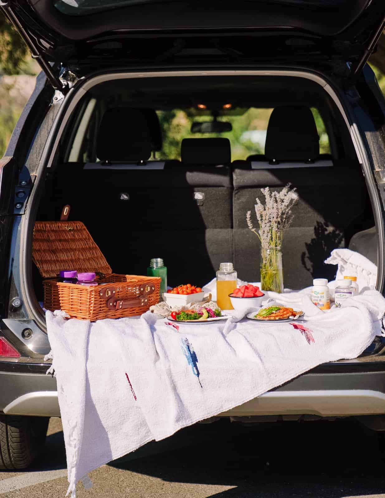 The back of a vehicle with a picnic on a picnic blanket. 