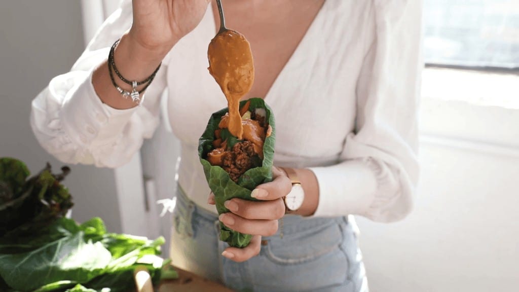 Maria pouring peanut sauce into collard green wraps