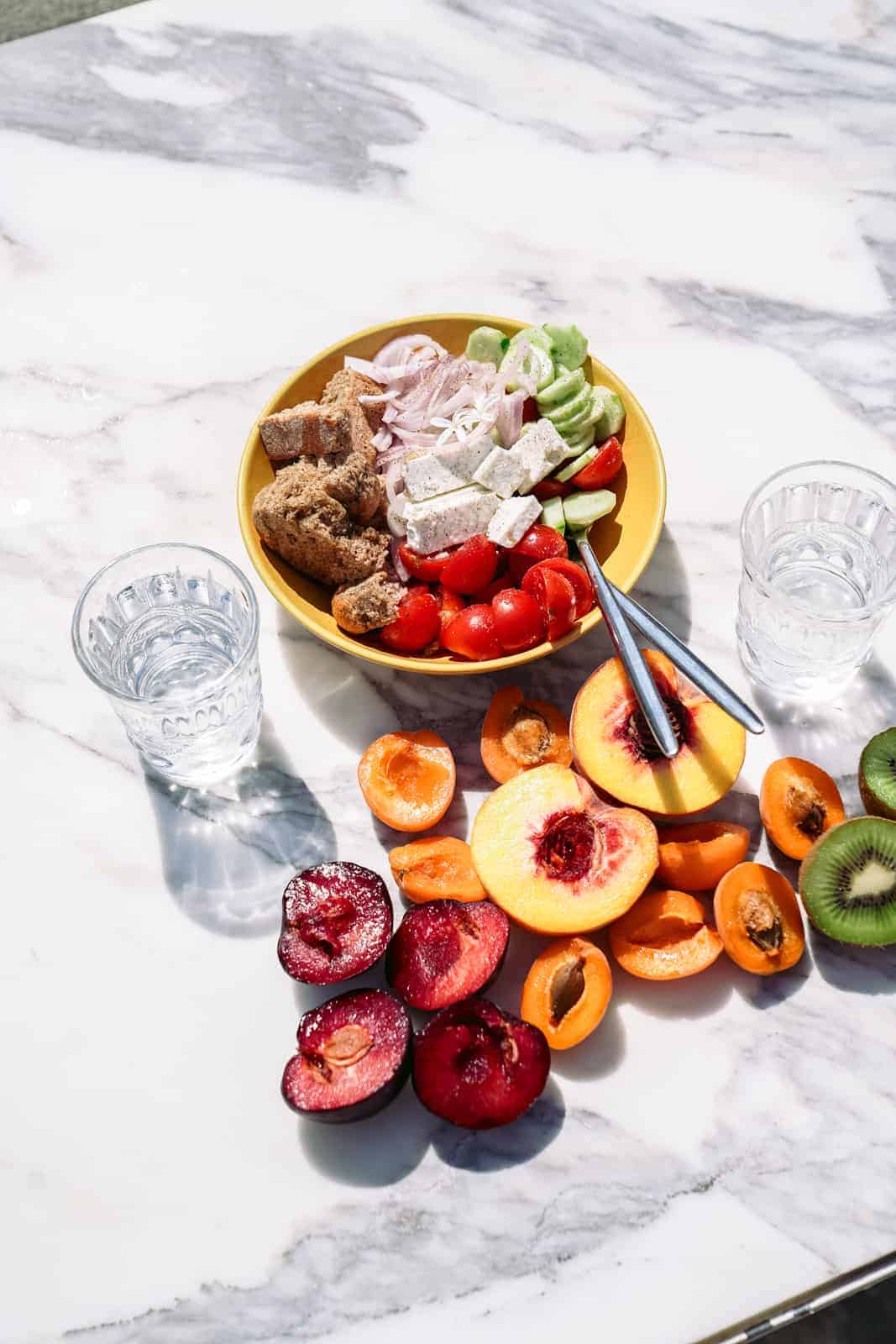 Yummy greek salad and fruits on white countertop in Greece.