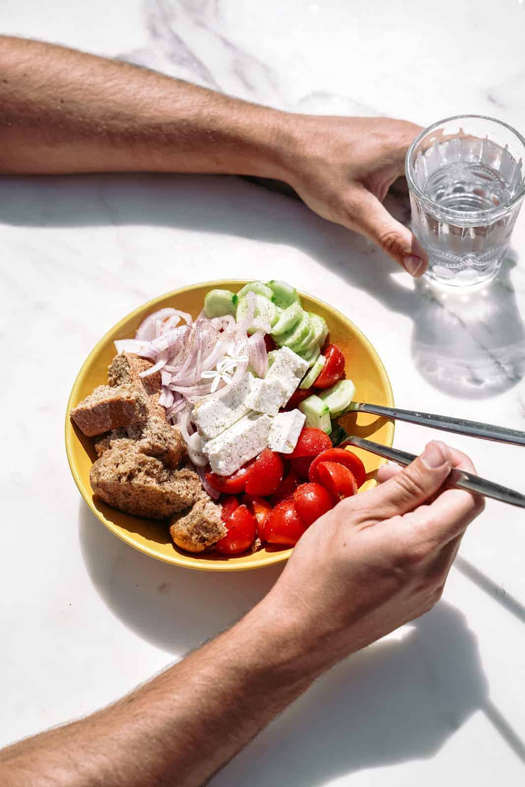 A healthy Greek salad sitting on a table with a glass of water.