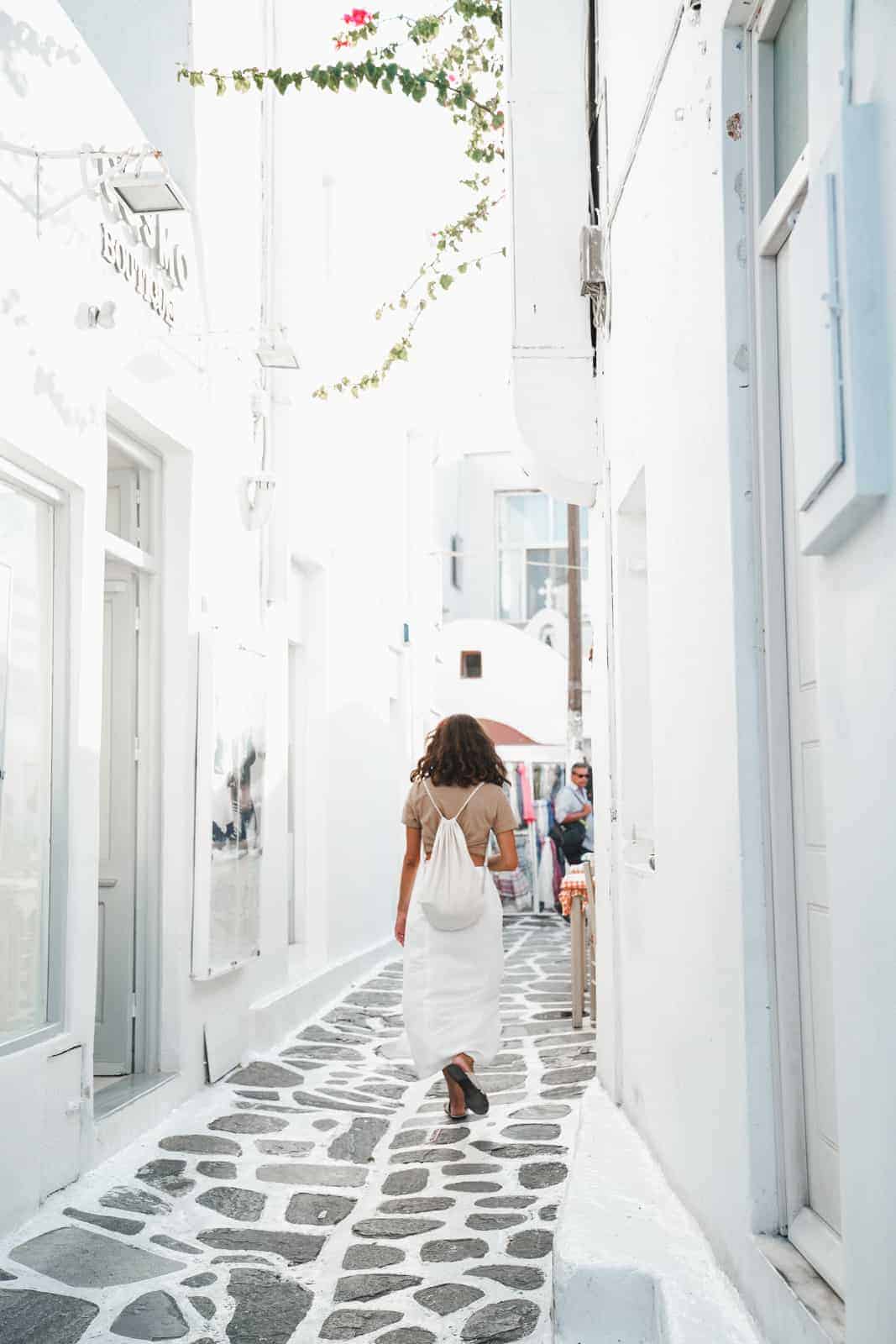 Maria of FoodByMaria walking the streets of Mykonos with a backpack on, one of her international travel tips.