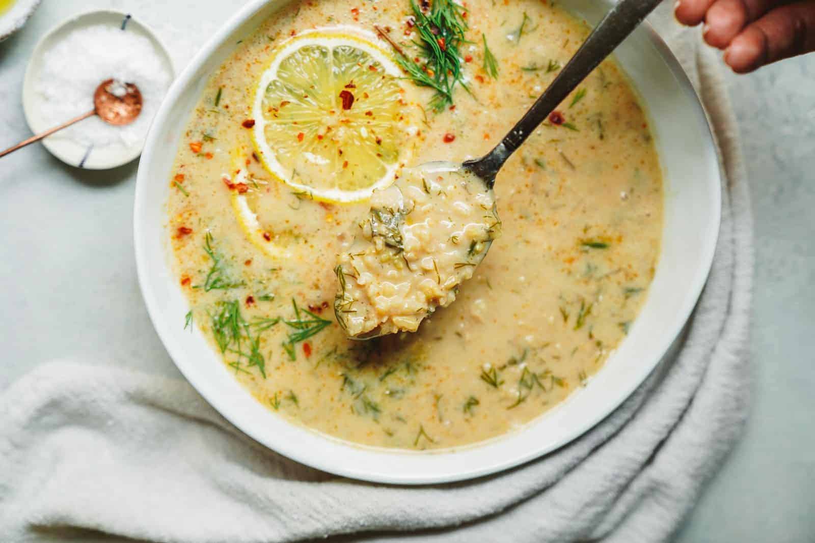 A spoon digging into a Creamy Vegan Lemon Rice Soup bowl (avgolemono)