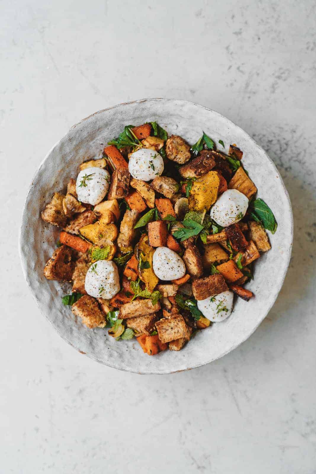 A bowl of Vegan Vegetable Panzanella Salad on a white table.