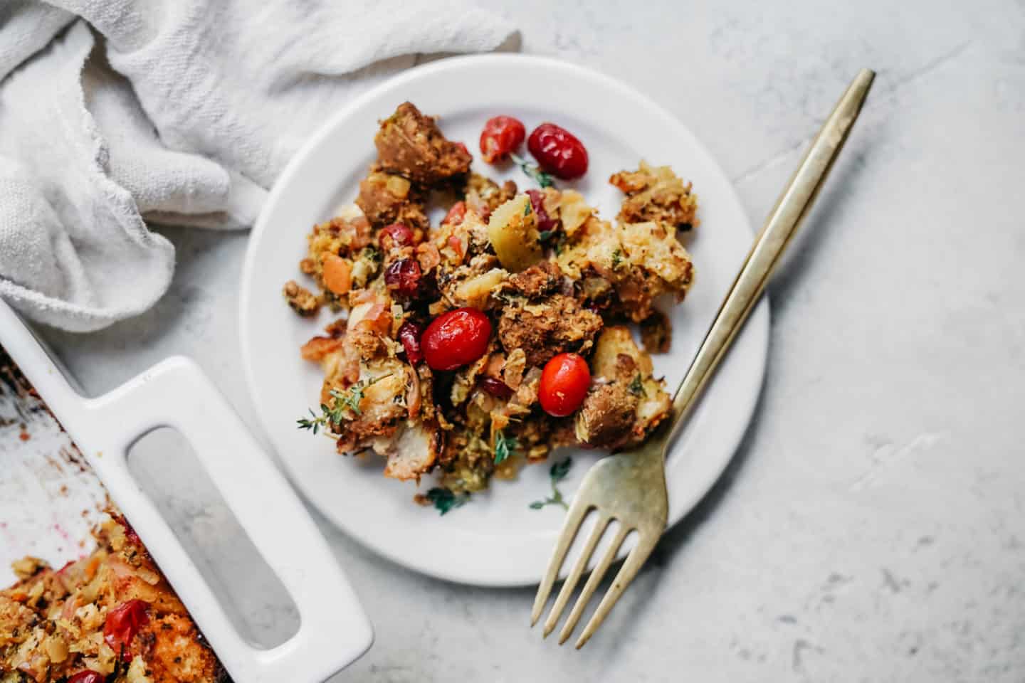 White plate with a serving of vegan stuffing on it with pops of red from the fresh cranberries.