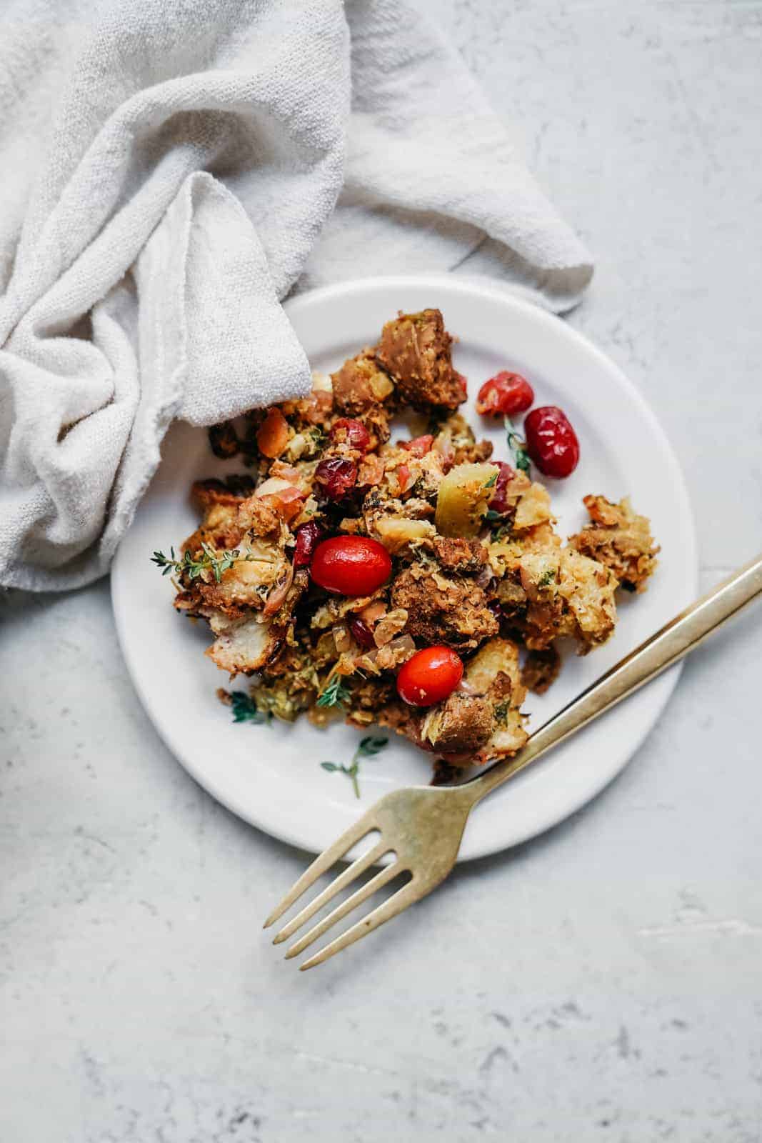 White plate with a serving of vegan stuffing on it with pops of red from the fresh cranberries.