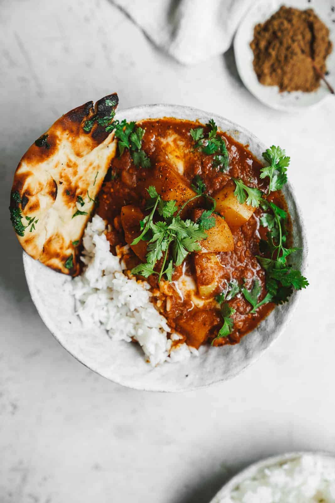 Big bowl of this creamy Vegan Butter Chicken recipe on table with naan bread.