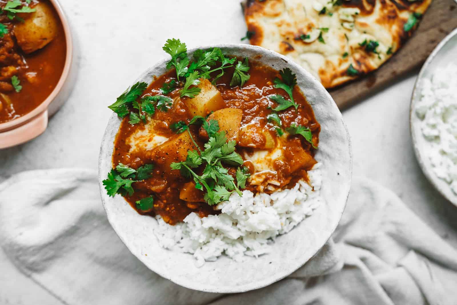 Vegan Butter Chicken in white bowl on top of fresh rice with a side of naan bread.