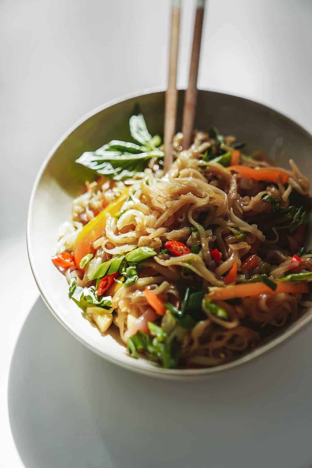 Close-up white bowl filled with this drunken noodles recipe with chopsticks.