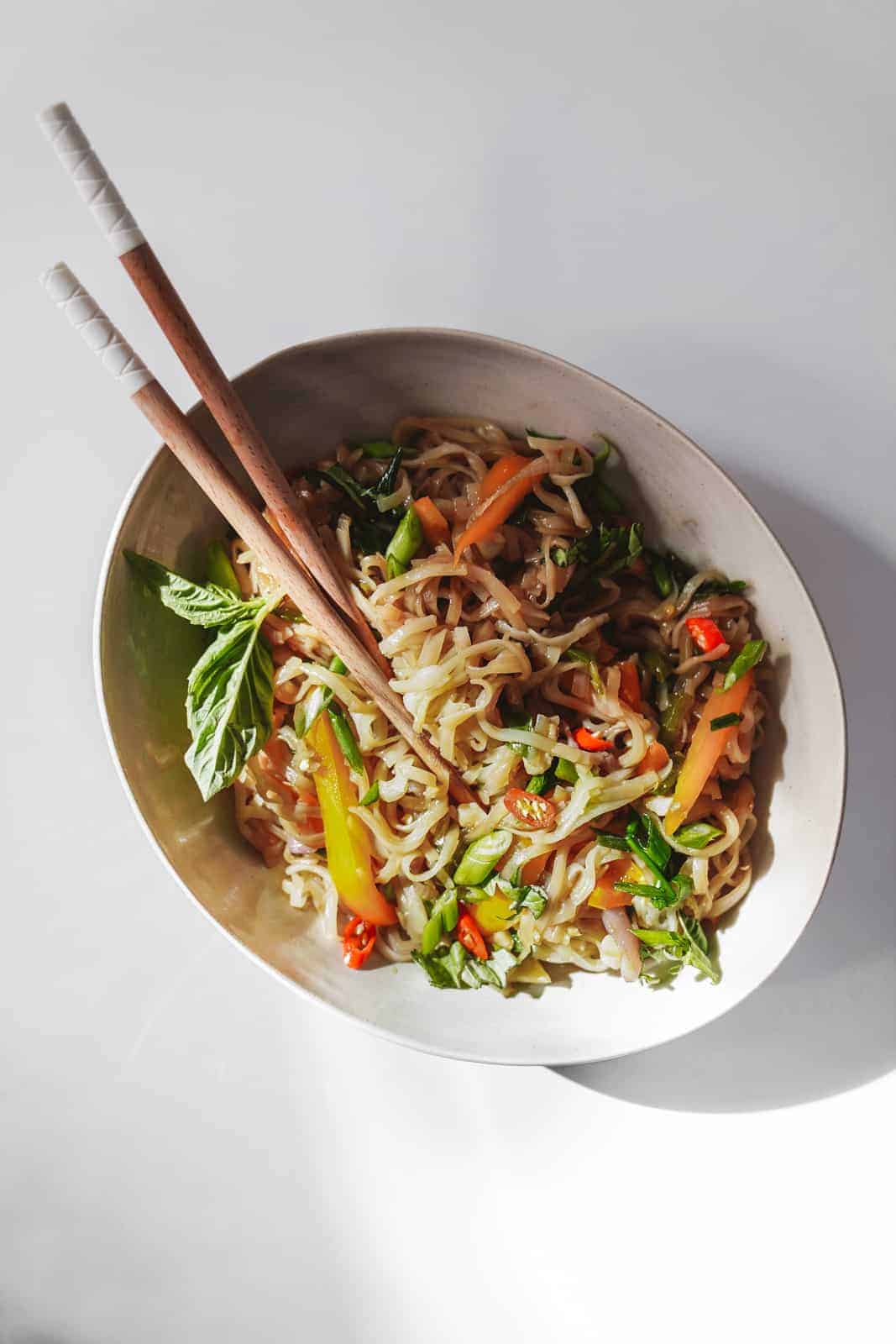 White bowl filled with this drunken noodles recipe with chopsticks.