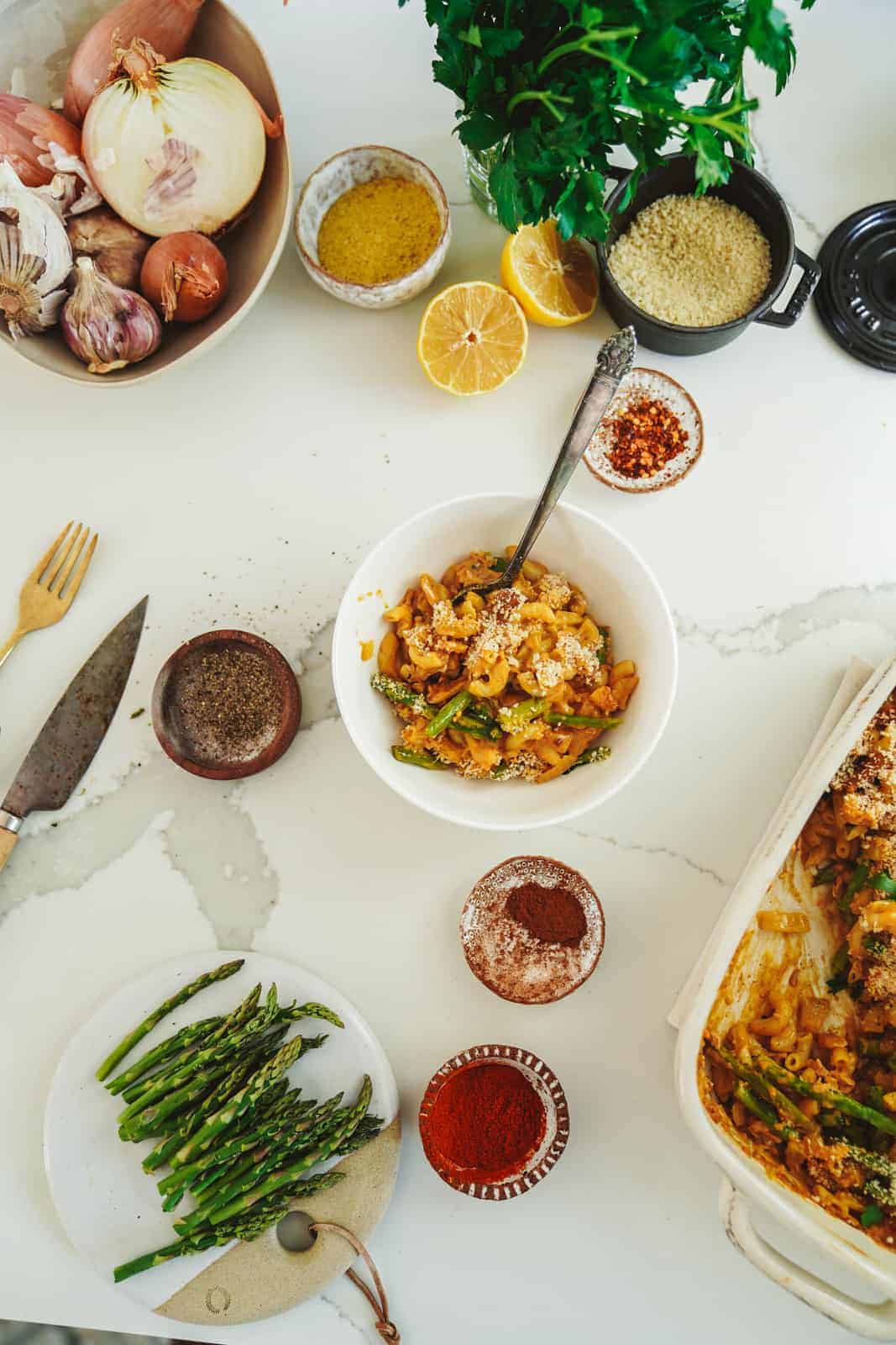 Creamy vegan casserole sitting in bowl surrounded by fresh ingredients and spices.