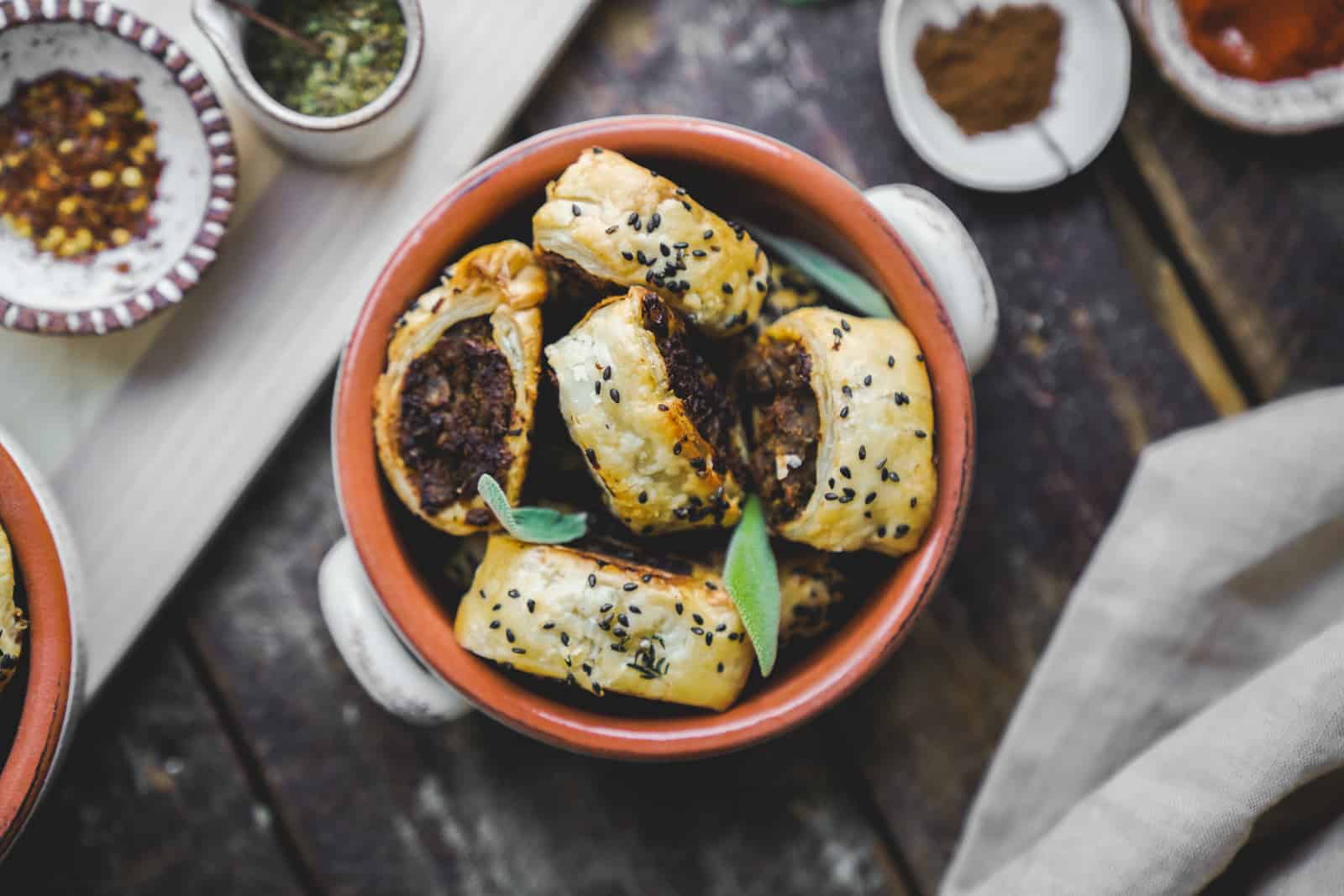 Bowl of vegan sausage rolls surrounded by spices. 