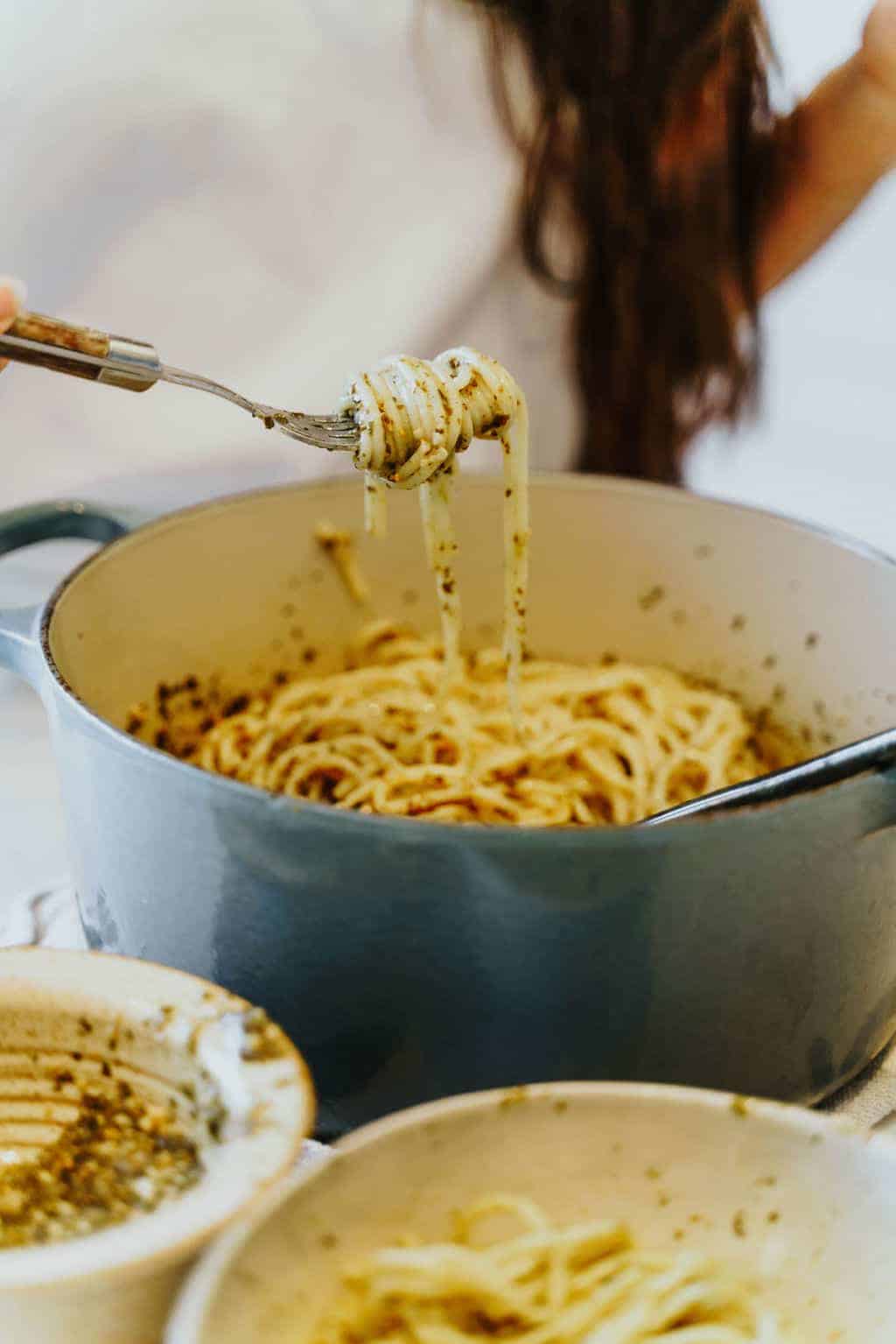 Twirling spaghetti noodles in a large pot with pesto sauce.