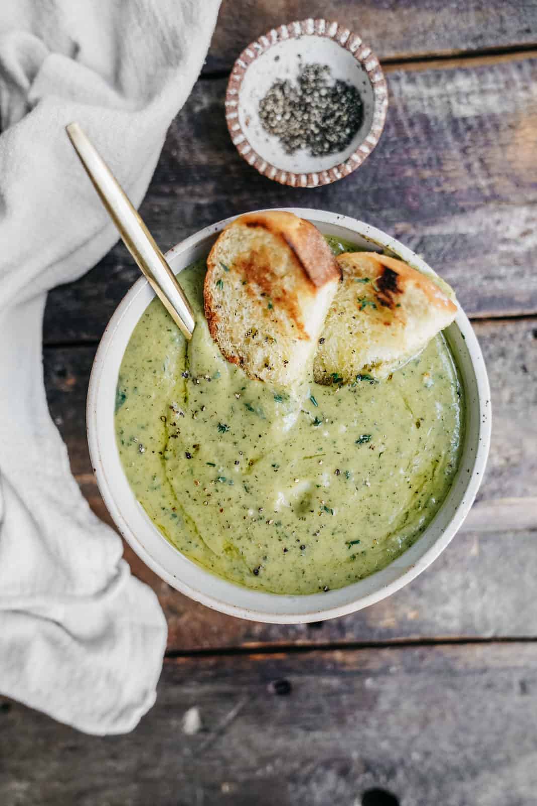One big creamy bowl of Broccoli Soup ready to eat with a drizzle of olive oil and toasted bread.