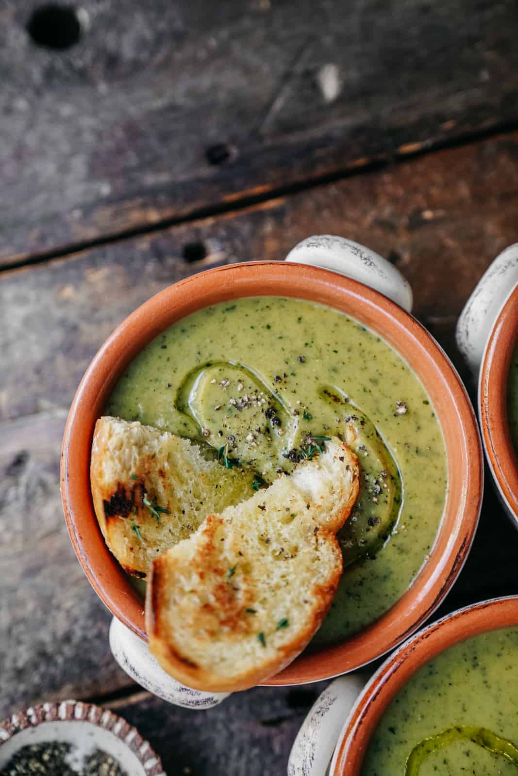 A comforting bowl of Broccoli Soup sitting on wooden table and topped with 2 slices of toasted bread.