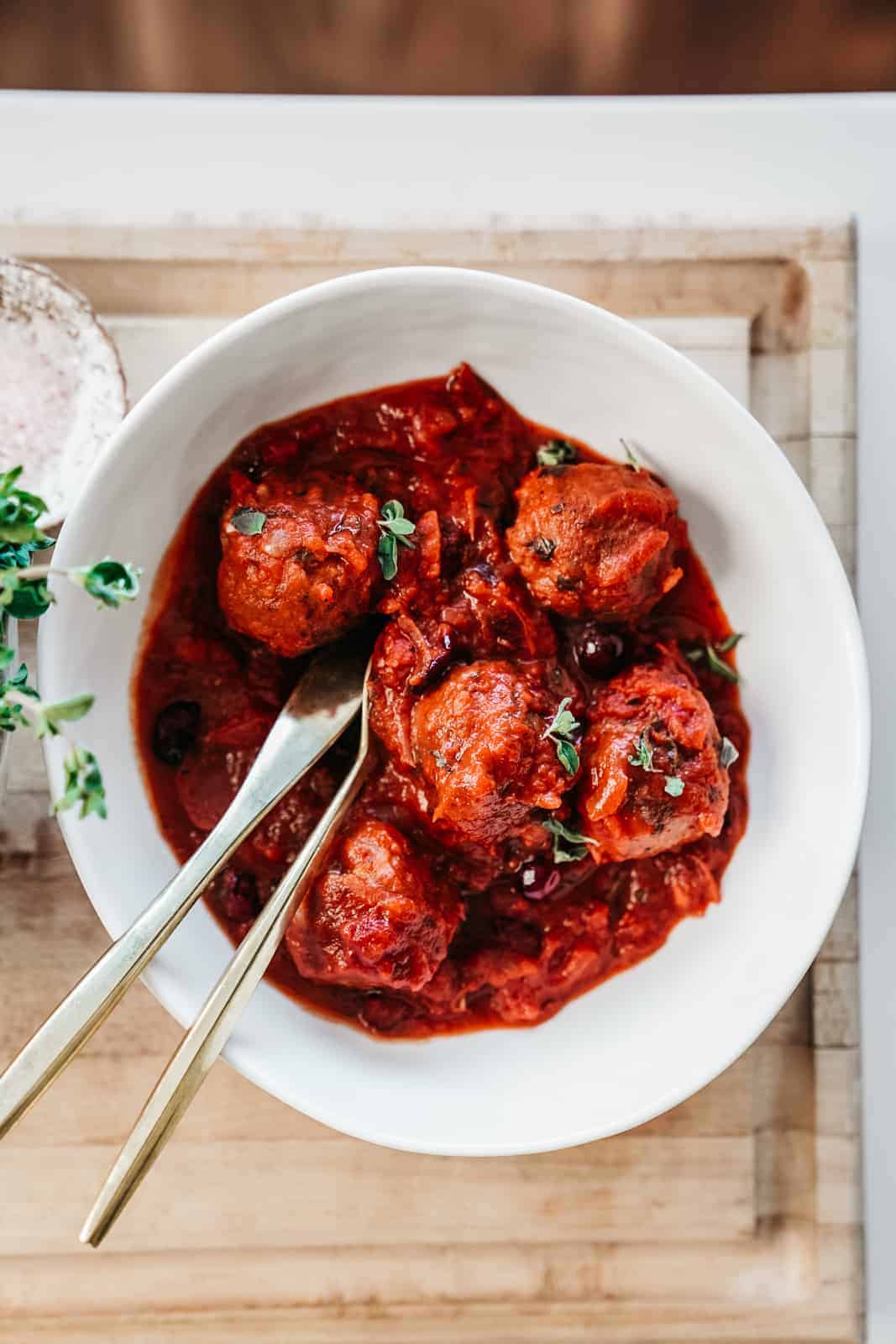 Yummy cranberry vegan meatballs in a white bowl sitting on a cutting board with serving utensils.