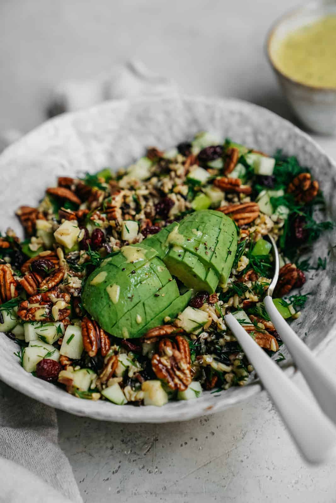 Easy Vegan Simple Wild Rice Salad sitting on counter with serving spoons in the dish and deliciously ripe avocado. A perfect salad for high protein vegan meal prep.