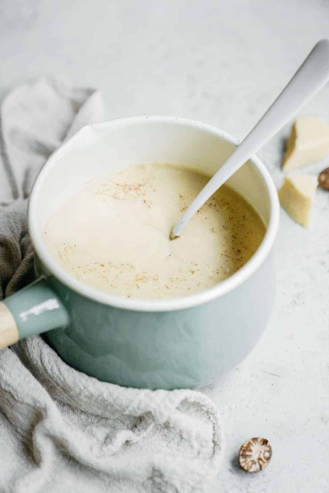 Vegan Bechamel Sauce sitting in a pot with a spoon on a counter.