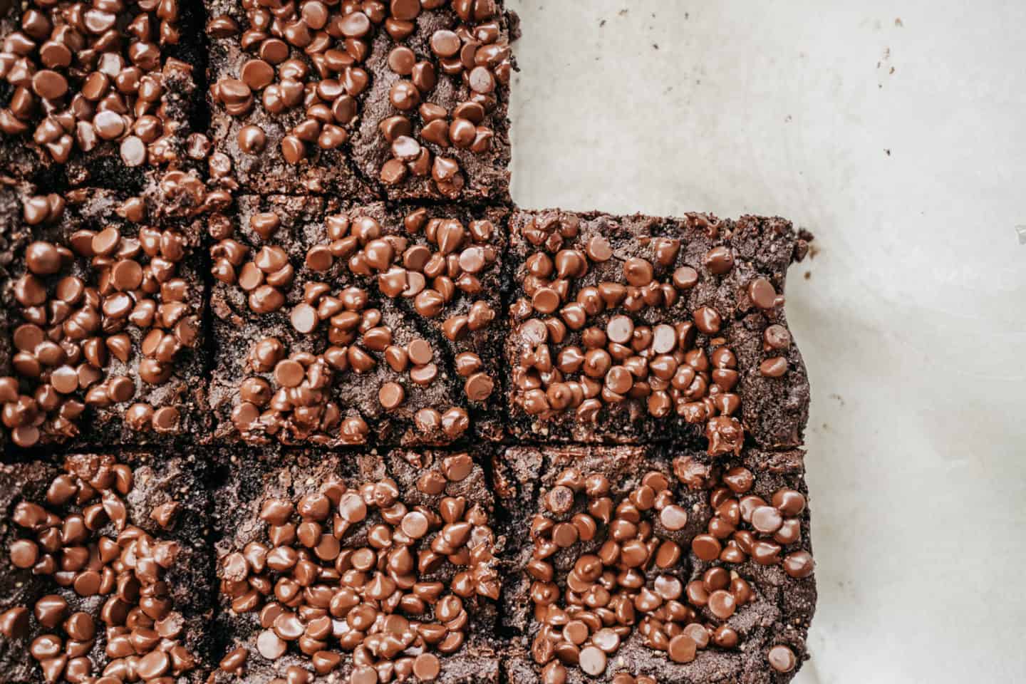 Vegan almond flour brownies on a countertop with chocolate chips on top and one piece missing