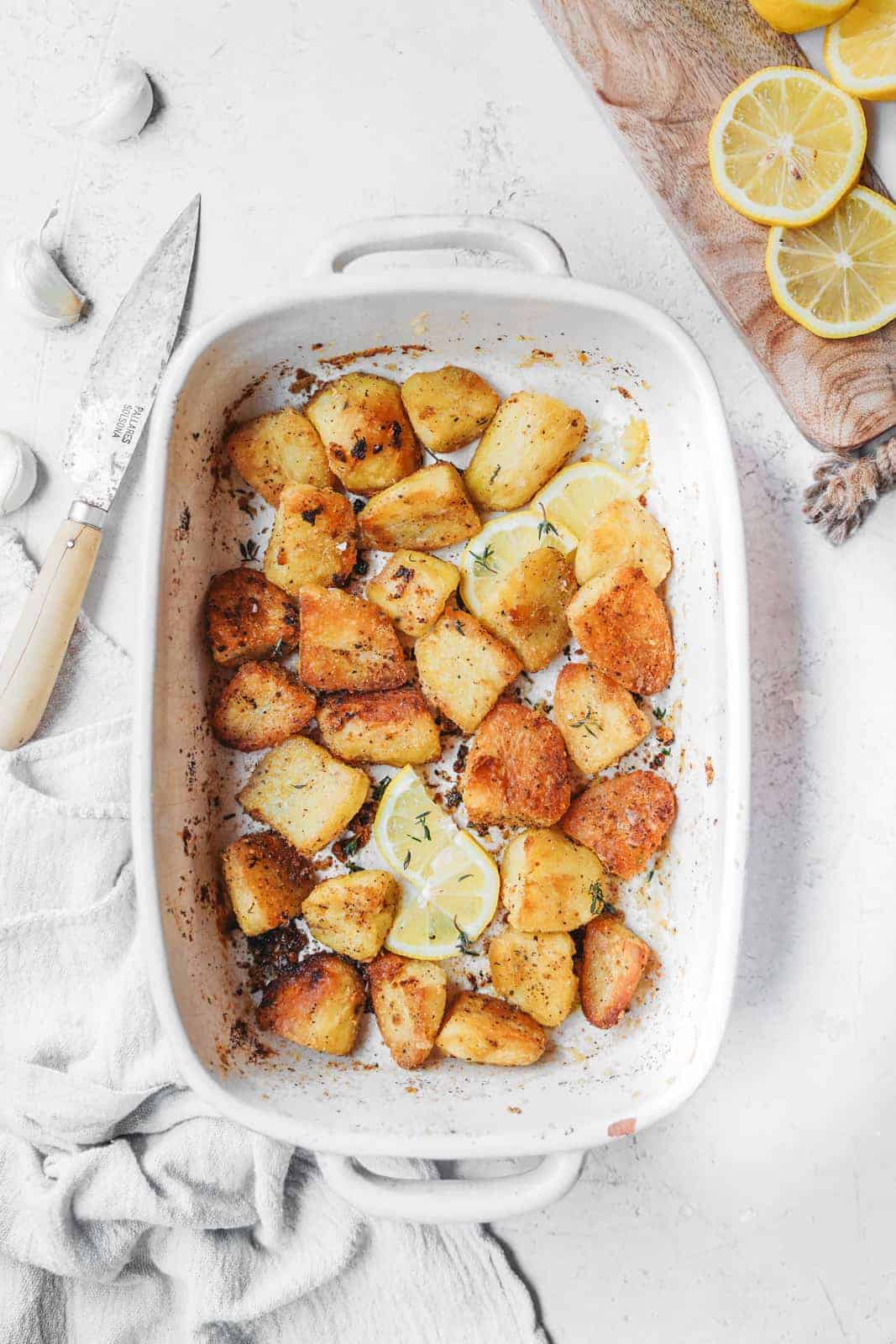 Baking dish with the finished crispy roasted potatoes in it, thyme has just been added and potatoes are ready to serve.