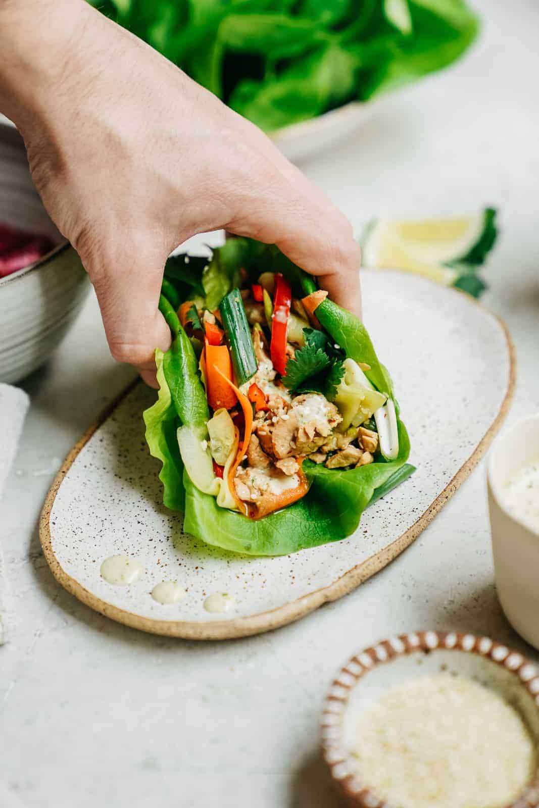 A hand grabbing a vegan tuna lettuce wrap off a plate.