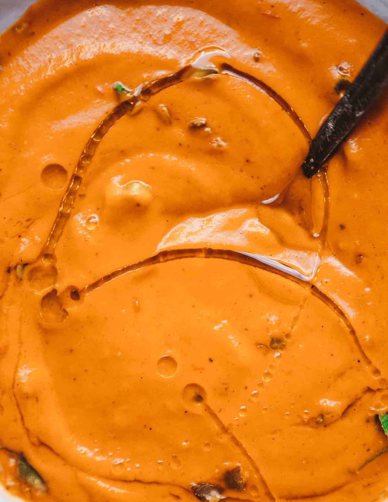 A close-up of creamy vegan carrot soup ready to be eaten with a drizzle of olive oil.