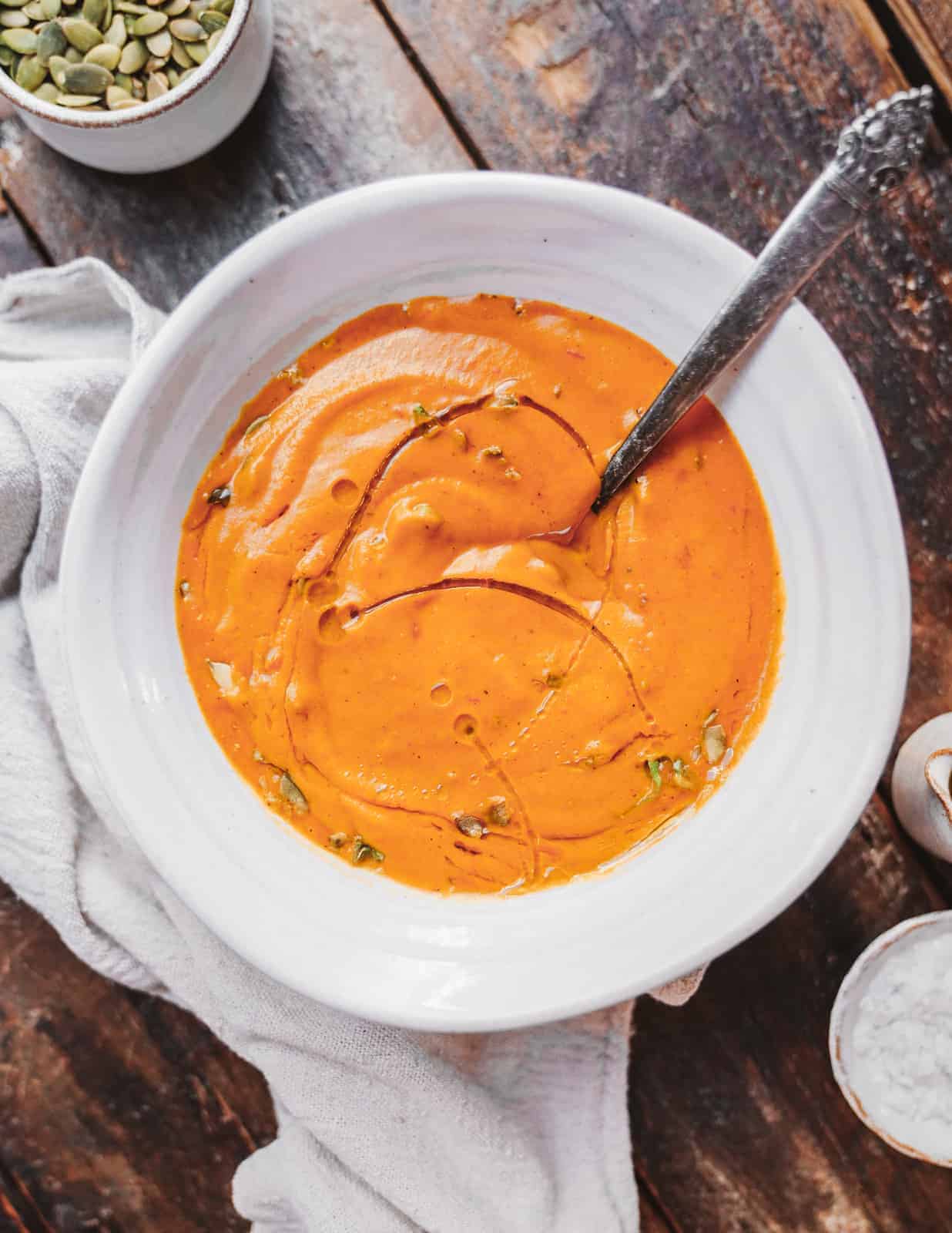 Creamy Carrot Soup Vegan and Delicious in a white bowl with a spoon, ready to be eaten.