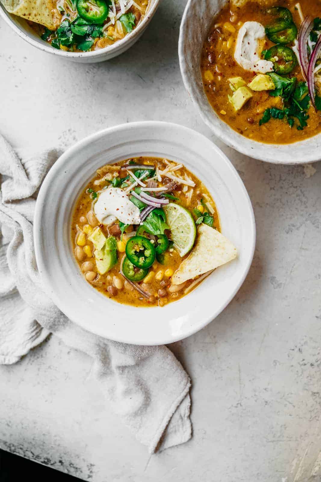 Big bowl of Vegan White Bean Chili sitting on table loaded with all the fixings.