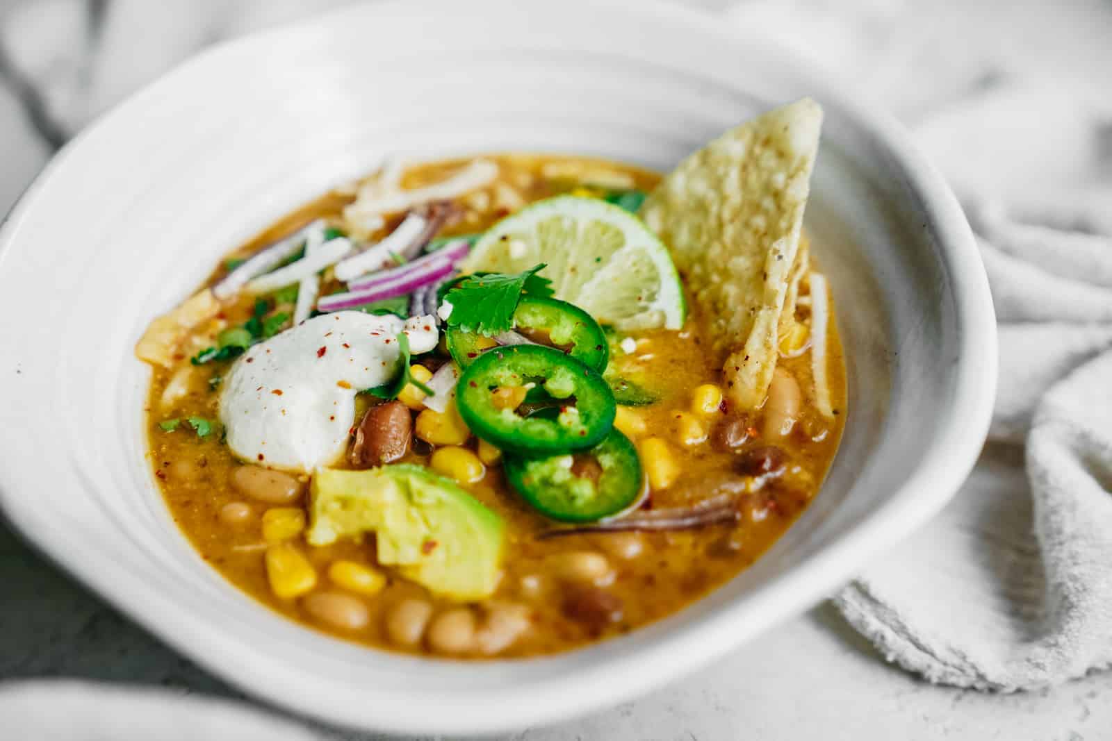 Big bowl of Vegan White Bean Chili sitting on table loaded with all the fixings.