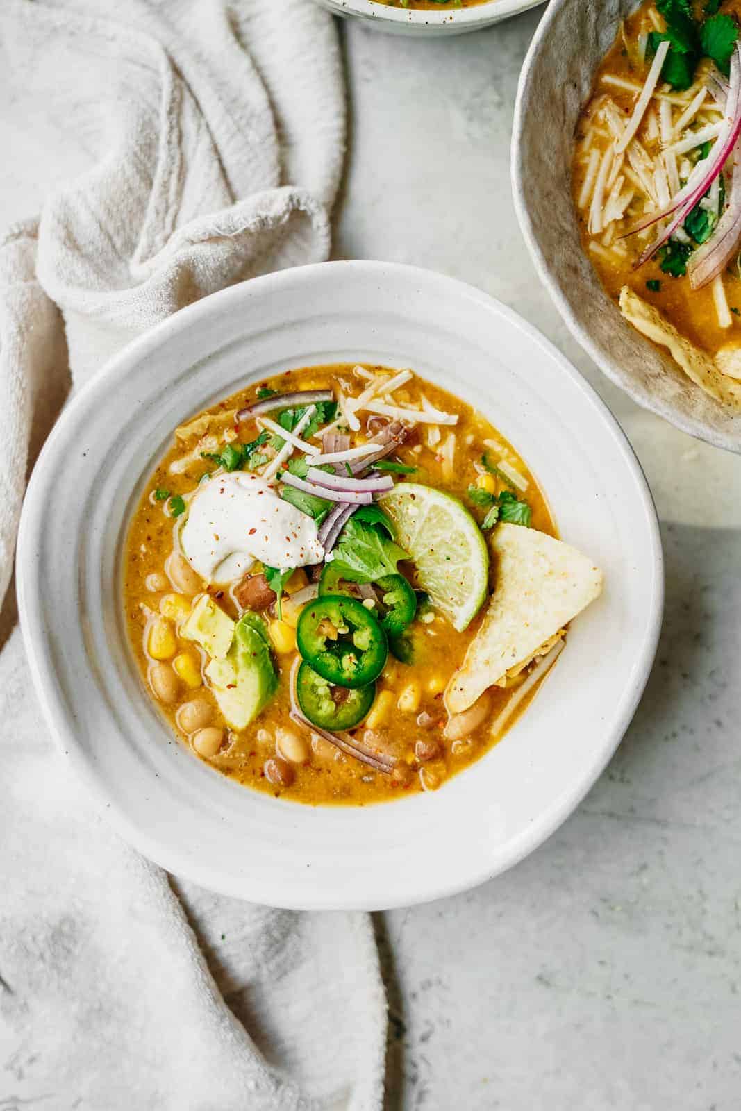 Big bowl of Vegan White Bean Chili sitting on table loaded with all the fixings.