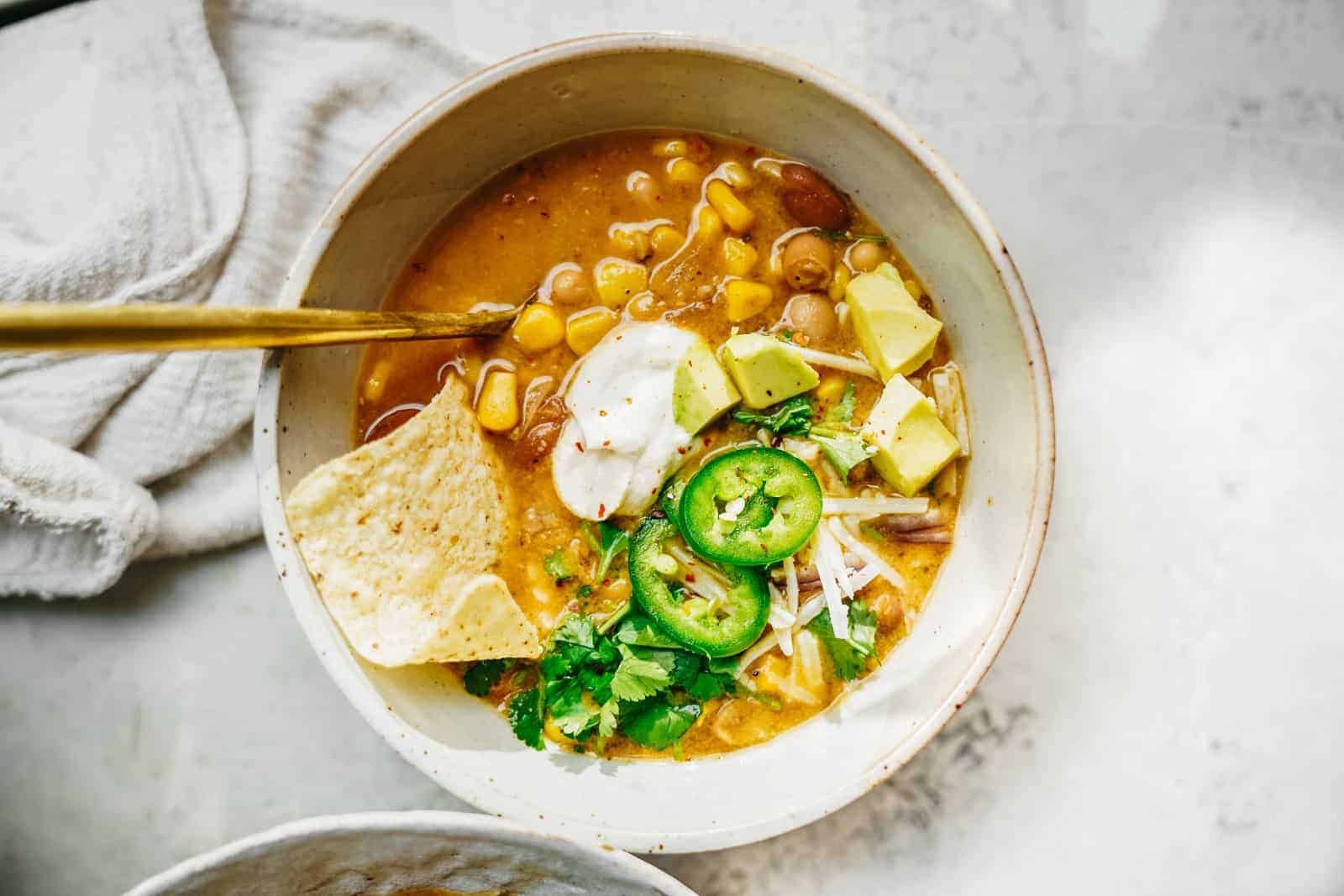 Big bowl of Vegan White Bean Chili sitting on table loaded with all the fixings.