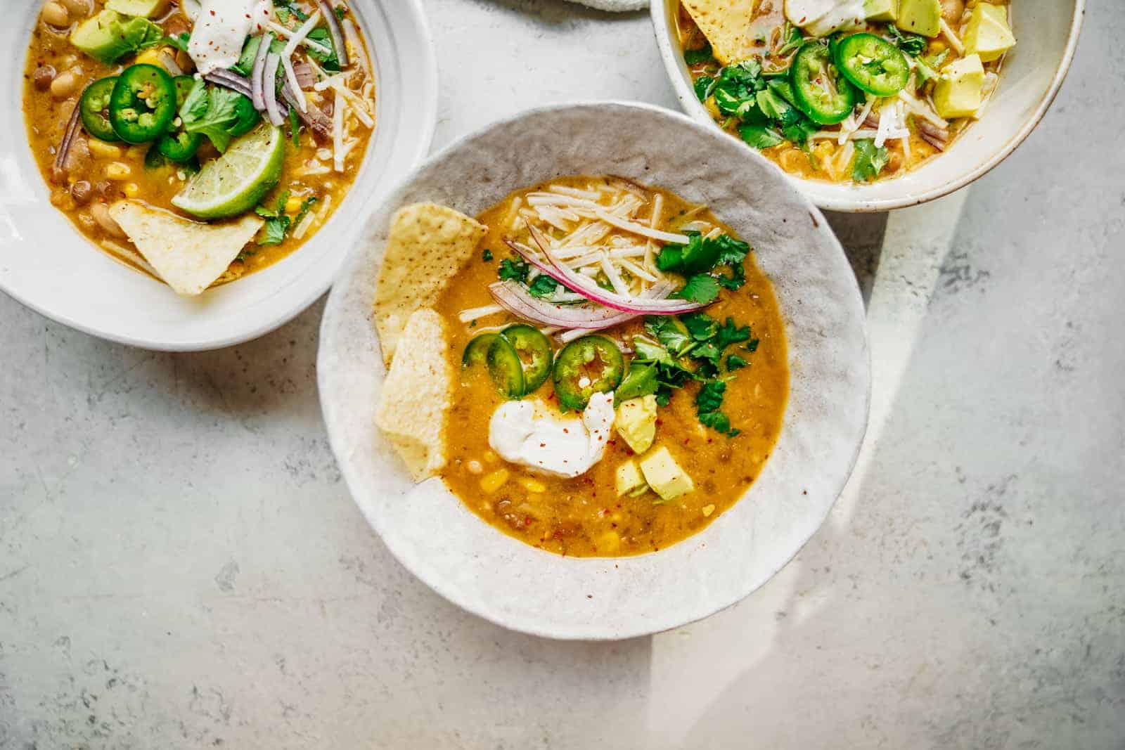 Big bowl of Vegan White Bean Chili sitting on table loaded with all the fixings.