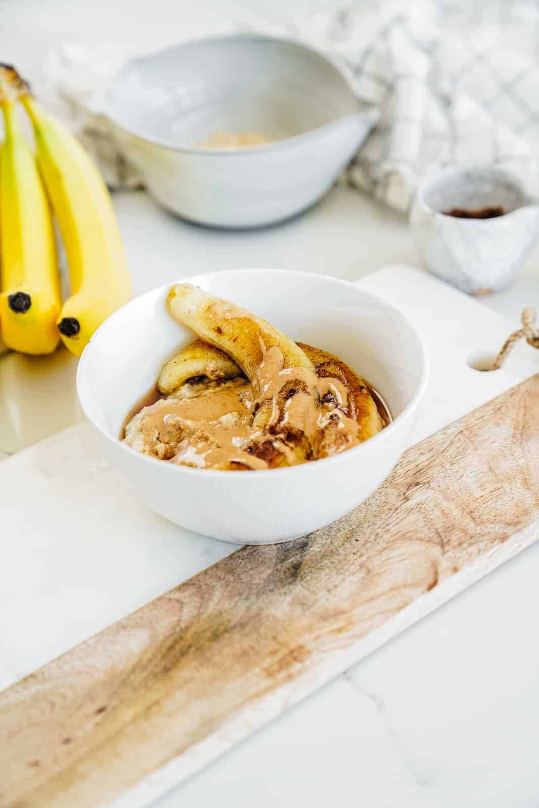 Countertop with bananas and bowl of fried banana recipe on top of oatmeal.