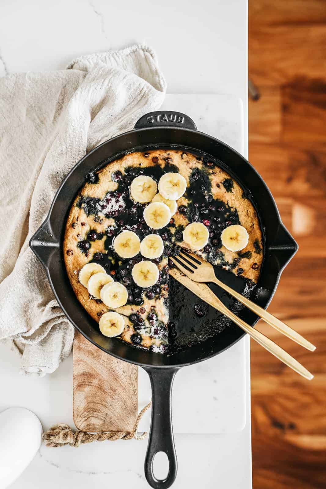 vegan blueberry pancakes skillet with fresh bananas cut on top.