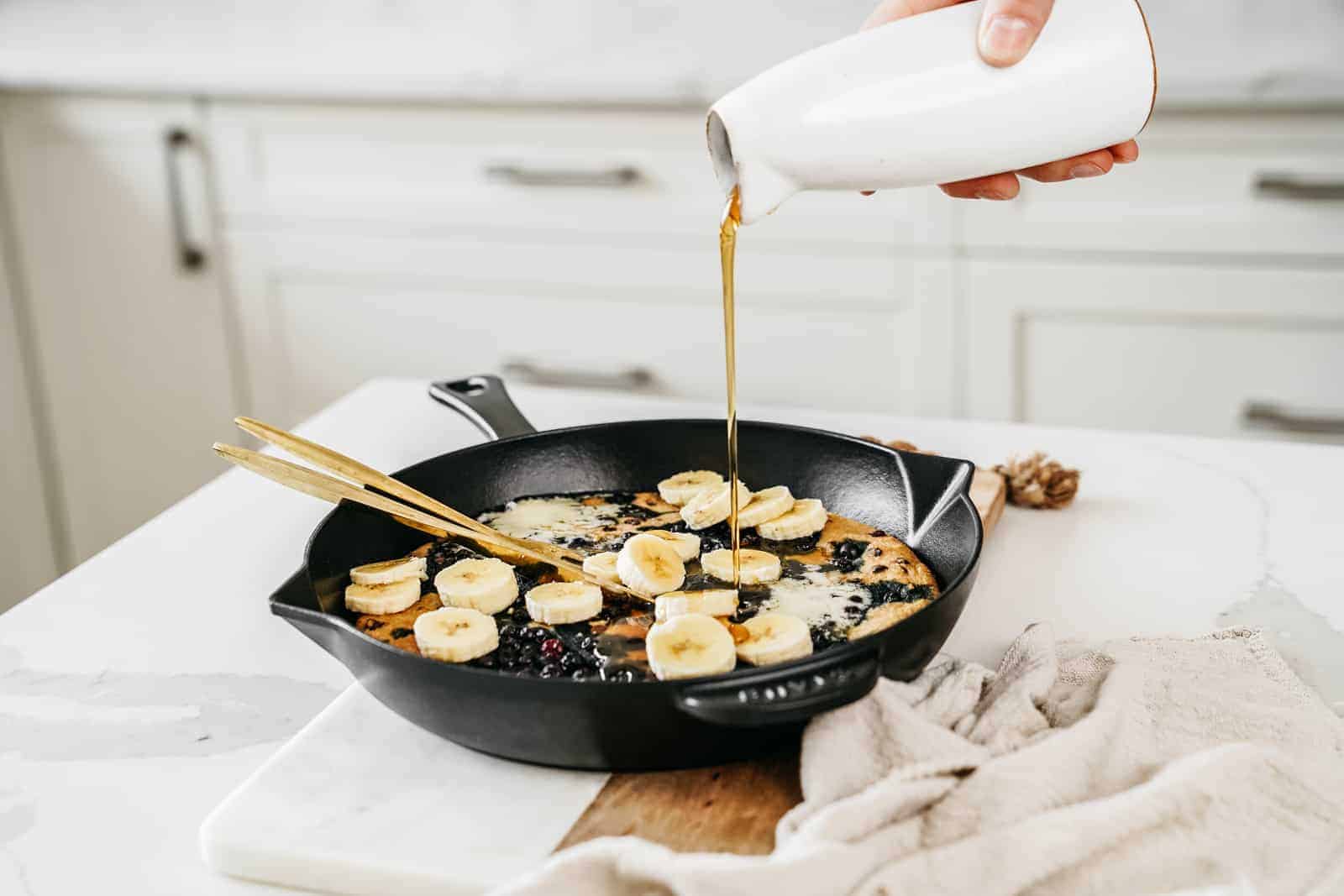 Maple syrup being poured on vegan blueberry pancakes in skillet.